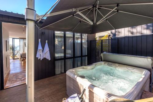 a hot tub on a deck with an umbrella at Wavesong - Stay Waiheke in Onetangi