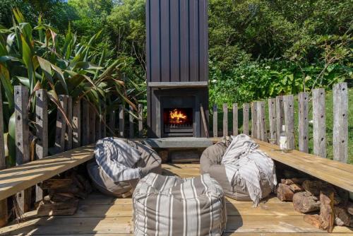 Una terraza de madera con dos pufs y una chimenea. en Miro Magic - Stay Waiheke, en Palm Beach