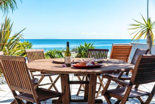 a wooden table with a bottle of wine and chairs at The Sands - Villa 28 - Stay Waiheke in Onetangi
