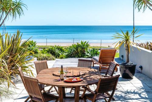 a wooden table and chairs on a patio with the beach at The Sands - Villa 28 - Stay Waiheke in Onetangi