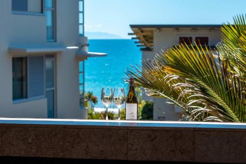 a bottle of wine and two glasses sitting on a ledge at The Sands - Apartment 12 - Stay Waiheke in Onetangi