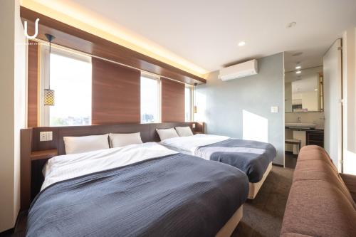 two beds in a hotel room with a couch at unito hotel residence Kyoto Station North in Kyoto