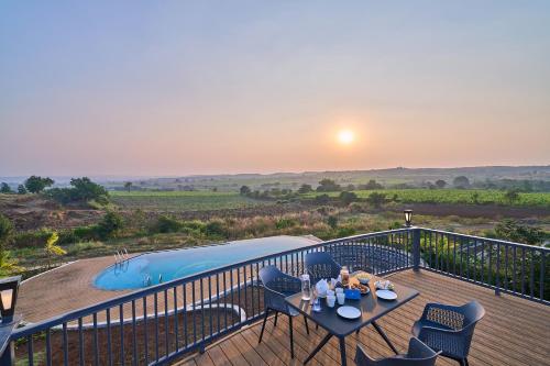 een terras met een tafel en stoelen en een zwembad bij SaffronStays Ashfield - 5BHK Eco-Farmhouse with Pools, Jacuzzi, Lawn & Games Room in Nashik