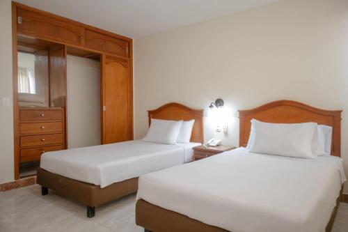 two beds in a hotel room with white sheets and a night stand at Hotel Faranda Bolivar Cucuta, a member of Radisson Individuals in Cúcuta