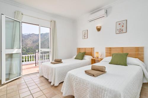 2 letti in una camera bianca con balcone di Villa Grayce a Frigiliana