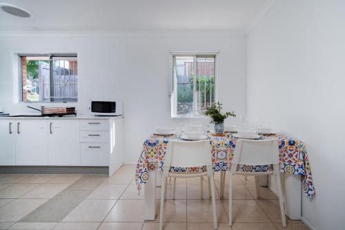 a white kitchen with a table and chairs at 3BR Cozy Sunnybank Hills Home in Brisbane