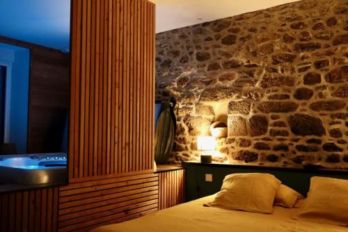 1 dormitorio con pared de piedra, 1 cama y bañera en La parenthese, en Beaussais sur Mer