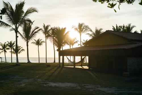 Pousada e camping Filó Caraíva في بورتو سيغورو: شاطئ فيه نخيل ومبنى والمحيط