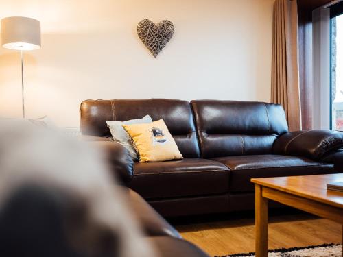 The Barn في Girthon: أريكة جلدية بنية اللون في غرفة المعيشة مع قلب على الحائط