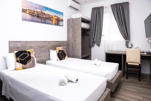 Napoli Suites Studios Aparthotel في سانت جوليانز: غرفة فندق بها سريران ومكتب