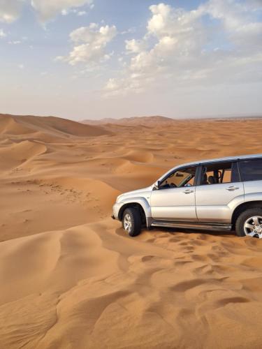 a white suv driving through the desert at Desert Pearl Camp in Merzouga