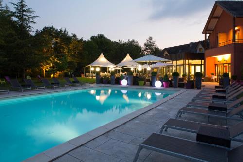 una piscina con sillas y sombrillas por la noche en Le Dracy Hôtel et Spa, en Dracy-le-Fort