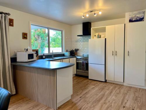 a kitchen with white cabinets and a white refrigerator at Sunshine cosy retreat in Hanmer Springs