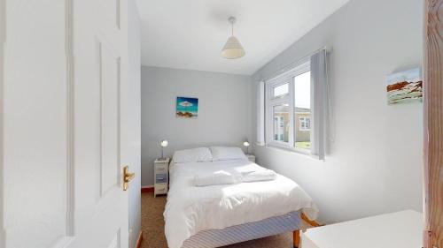 a white bedroom with a bed and a window at C23 Wilmar, Riviere Towans in Hayle