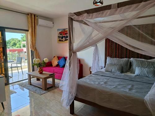 Les Studios de l'Oasis في Ngaparou: غرفة نوم مع سرير مظلة وأريكة