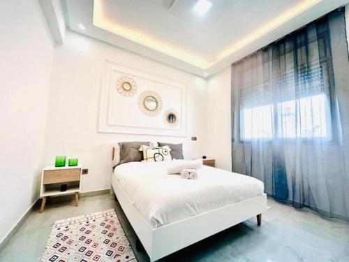 Una habitación blanca con una cama y una ventana en Elegant 3BR Stay 5min to Hay Riad, en Temara