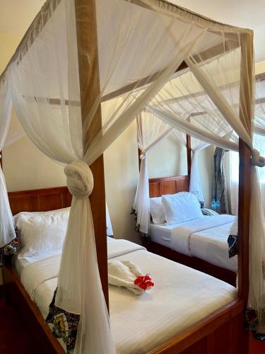 two beds in a bedroom with white sheets and a canopy at Patamu Restaurants Lodge & Safaris in Karatu