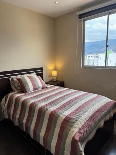 a bedroom with a bed with a striped blanket and a window at 7th floor Live, Laugh and Relax in Cochabamba