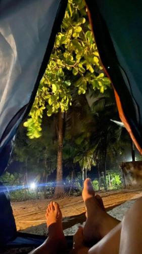 uma pessoa com os pés para cima em uma barraca com uma árvore em camping do point lá na barra em Amontada