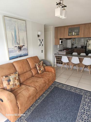 uma sala de estar com um sofá marrom e uma cozinha em Parque Mar Depto em El Tabo