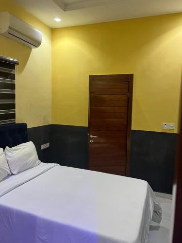 1 dormitorio con cama blanca y puerta marrón en The Private Pearl Apartment, en Ikeja
