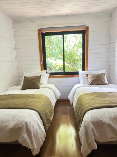 Dos camas en una habitación con ventana. en Cabañas Alto del Bosque, en Coñaripe