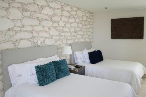 Casa Diamante Hotel Boutique - Mineral de Pozos في Mineral de Pozos: غرفة فندقية بسريرين وجدار حجري