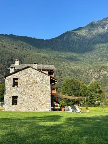 Chalet Valchiavenna في San Cassiano: بيت حجري في حقل فيه جبال في الخلف