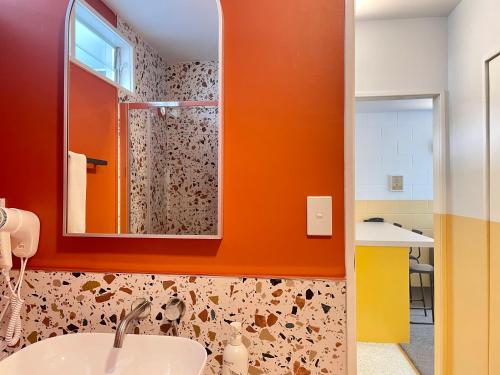 Mount Eden Motel في أوكلاند: حمام برتقالي مع حوض ومرآة