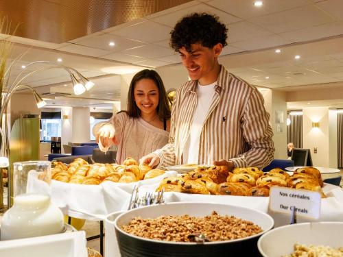 un hombre y una mujer parados frente a un buffet de comida en Mercure Rouen Centre Cathédrale, en Rouen