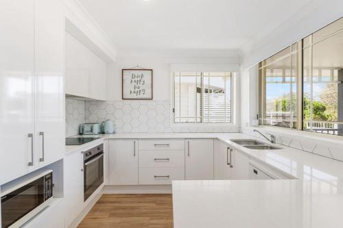 a white kitchen with white cabinets and a window at Spades - at Lighthouse Beach in Port Macquarie