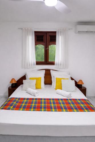 a white bedroom with a large bed with yellow pillows at Domaine de Lauréal in Le Moule
