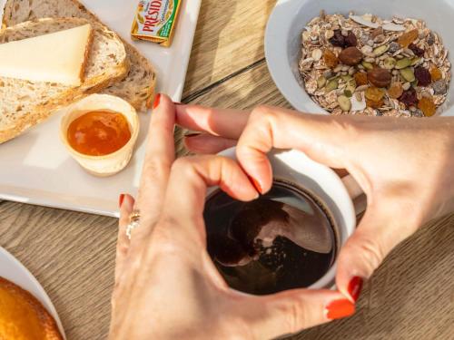 a woman holding a cup of coffee with a plate of food at ibis Ciboure Saint-Jean-de-Luz in Ciboure