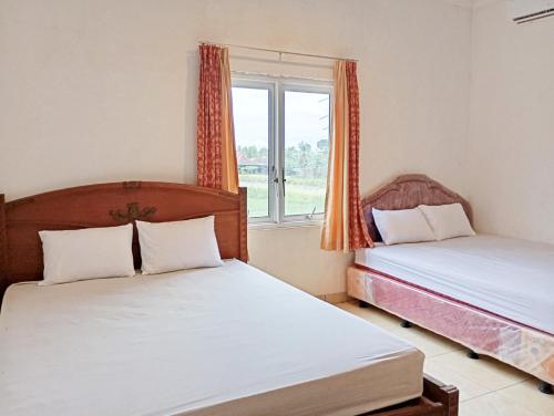 twee bedden in een kamer met een raam bij Hotel Intan Sampang Banyumas RedPartner 