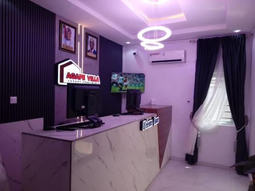 Agape Villa Luxury Apartments في بنين سيتي: غرفة بها مكتب استقبال مزود بتلفزيون ومنضدة