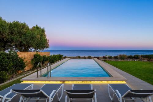 a swimming pool with chairs and the ocean in the background at Sea Homes Villas-Villa Sylvia in Kiotari