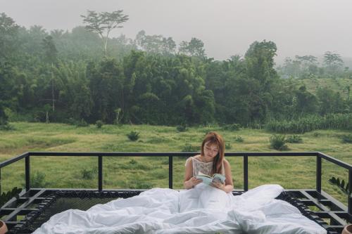 ein Mädchen sitzt auf einem Bett und liest ein Buch in der Unterkunft Khaosok River Stone Resort & Camp in Ban Thung Lang Tham