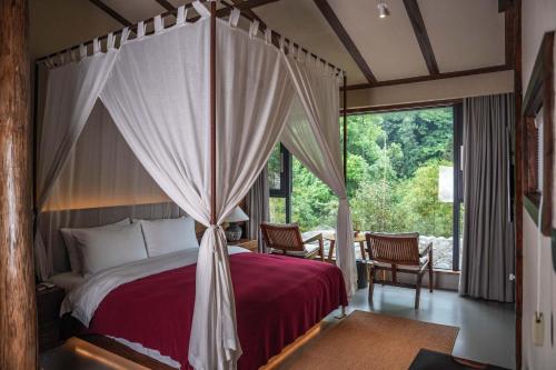 ein Schlafzimmer mit Himmelbett und großem Fenster in der Unterkunft Relais & Châteaux Su Shien Valley Hotel in Dujiangyan