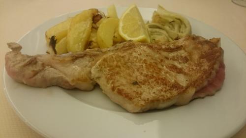 a plate of food with meat and potatoes and lemon slices at Hotel Bristol in Lignano Sabbiadoro