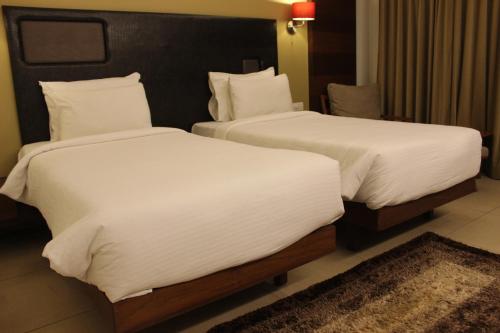 two beds with white sheets in a hotel room at Hotel Cosmopolitan in Ahmedabad