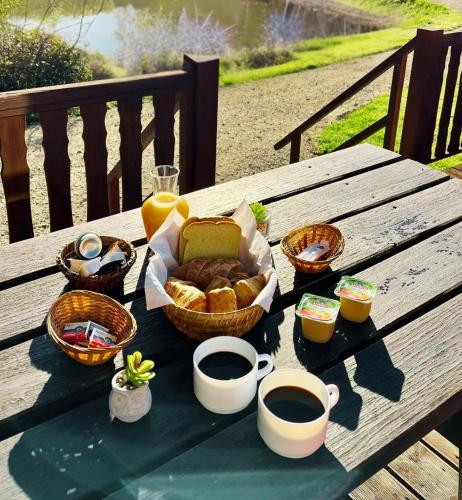 een picknicktafel met een mand brood en kopjes koffie bij SAS Le Hameau des Grilles in Saint-Fargeau