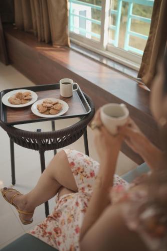 Una mujer sentada junto a una mesa con dos tazas de café. en High Five Hotels, en Assagao