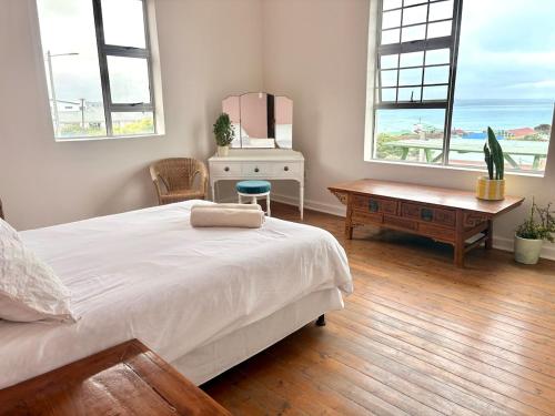 a bedroom with a bed and a table and windows at Sunrise & Sunset Haven in Mossel Bay