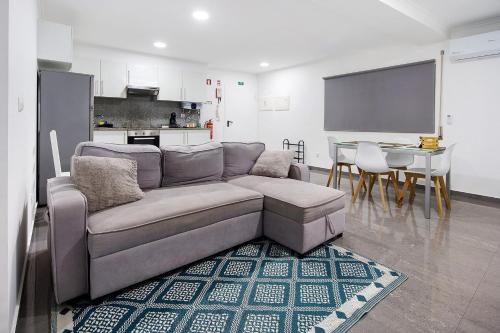 a living room with a gray couch and a kitchen at Windmill Açores Suite in Furnas
