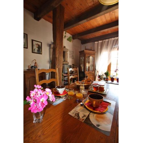a dining room table with a vase of pink flowers on it at Maison d'Hôtes LA JEANCOISE in Nonville