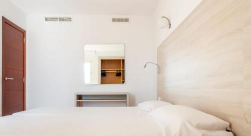 a white bedroom with a bed and a mirror at MallorcaRooms Cala Millor in Cala Millor