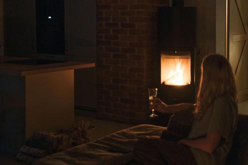 Rumiane pola - stodoła na Mazurach z widokiem na jezioro في Brajniki: امرأة تجلس أمام المدفأة ليلاً