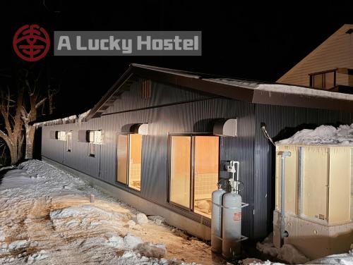 un edificio con luces encendidas en la nieve por la noche en A Lucky Hostel, en Hakuba
