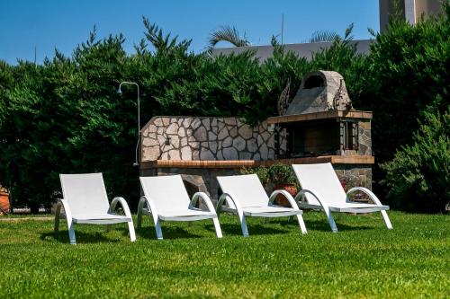 four white chairs sitting in the grass in front of a fireplace at Seascape Villa in Afantou
