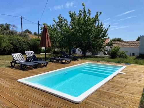 a swimming pool on a deck with two chairs and an umbrella at QUINTA DAS TEIMOSAS by Stay in Alentejo in Cercal